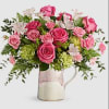 Pink roses and white flowers arranged in a glass pitcher vase