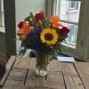 Bouquet of sunflowers, red roses, orange lilies, and purple filler in a glass vase