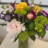 Mixed bouquet of yellow roses, pink peonies, and purple flowers in a glass vase