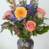 Mixed bouquet of pink, purple, and yellow flowers in a glass vase