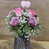 Pink roses with baby's breath in a purple glass vase, topped with a heart pick