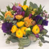 Round arrangement of yellow and purple flowers in a green glass vase