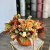 Orange floral arrangement in a pumpkin container with a ribbon