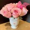 Pink roses arranged in a white face-shaped vase with a pink bow