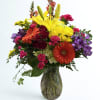 Bright yellow lilies and orange-and-yellow gerbera daisies create the immediate burst of