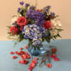 Bouquet of red roses, blue hydrangeas, and purple flowers in a glass vase