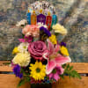 A glass cube filled with colorful blooms and a small Happy Birthday