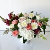An arrangement of fresh-cut flowers includes roses, dahlia, scabiosa, hydrangea, and snapdragon