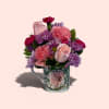 A compact cluster of soft pink carnations, pale pink roses, and vivid