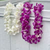 Two orchid leis draped over a white railing, one white and one purple.