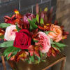 Low arrangement of red, pink, and peach roses with orange alstroemeria in a clear vase on a metal stand