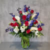 Tall bouquet of red roses, white calla lilies, and blue flowers in a glass vase