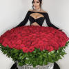 Large basket of red roses with green leaves, held by a woman in a black dress