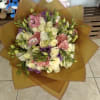 Mixed bouquet of pink, white, and purple flowers wrapped in brown paper