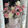 Pink and white roses arranged in a pale pink hatbox with ribbon.