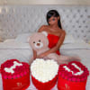 Three heart-shaped rose boxes with a teddy bear on a bed