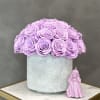 Lavender roses in a silver round box with a small pink figurine beside it