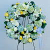 Large floral wreath with white lilies, yellow roses, and blue hydrangeas on a stand