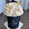 Cream and blush roses arranged in a black hat box with a gold crown topper.