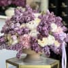 Lavender and white floral arrangement in a pedestal bowl with a ribbon