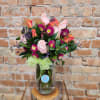 Pink roses and purple flowers arranged in a glass vase with a green ribbon.