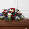 Low, spreading spray of red roses, white mums and blue delphinium to