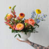 A joyful, garden-inspired arrangement in warm peach, coral, and golden tones, accented