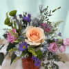 A medium sized arrangement with purple blooms and an orange rose to