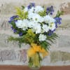 White daisies and blue flowers in a glass vase with a yellow ribbon