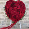 Heart-shaped red rose arrangement on a stand with a flowing ribbon