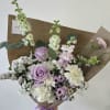 Hand-tied bouquet of lavender roses and white flowers wrapped in brown paper