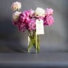 Pink and white bouquet in a clear glass vase with a hanging tag