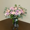 Pink roses and carnations arranged in a glass vase with a ribbon