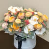 Pastel flower arrangement in a round white box with orchids and roses