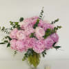 Large arrangement of pink peonies in a clear glass vase beside a small votive candle