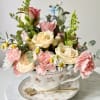 A tea cup filled with roses, carnations, and tiny white daisy-like blooms-this