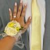 A delicate wrist corsage in soft cream-white roses and bright yellow accent