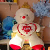Large teddy bear holding a heart pillow beside a vase of blue flowers