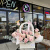 Pink roses arranged in a white basket with a LOVE ribbon
