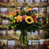 Mixed bouquet of orange, pink, yellow, and blue flowers in a glass vase