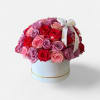 Round box arrangement of pink, lavender, and red roses with a ribbon bow