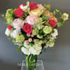 Mixed bouquet of pink, white, and green flowers in a tall glass vase