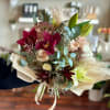 Bouquet of burgundy orchids, pale roses, and lilies wrapped in paper