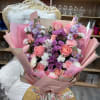 Hand-tied bouquet of pink roses, purple mums, and white and pink carnations wrapped in pink paper