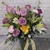Mixed bouquet of roses, lilies, and purple blooms in a glass vase