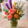 A lush, garden-style flower arrangement featuring roses, tulips, seasonal blooms, and decorative