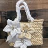 A handcrafted woven straw handbag trimmed with satin ribbon flowers and sparkling