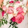Handheld bouquet of pink and white flowers with trailing greenery