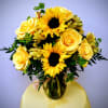 Yellow roses and sunflowers arranged in a glass vase