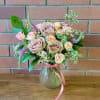 Bouquet of blush and peach roses in a glass vase with a pink ribbon